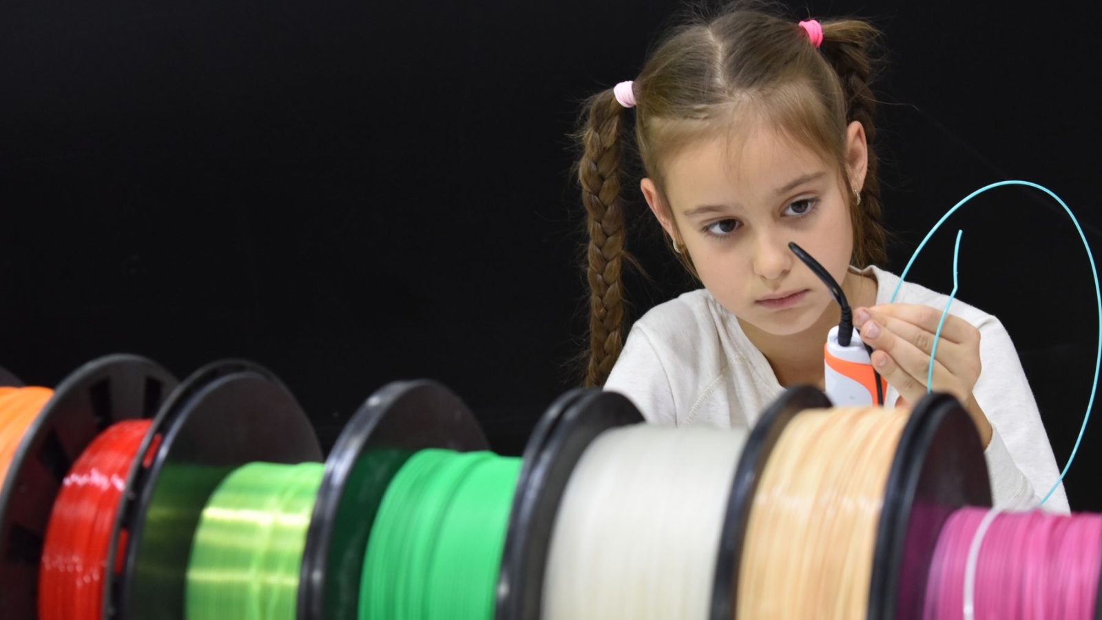 A focused girl with braided hair explores 3D printing using colorful filaments