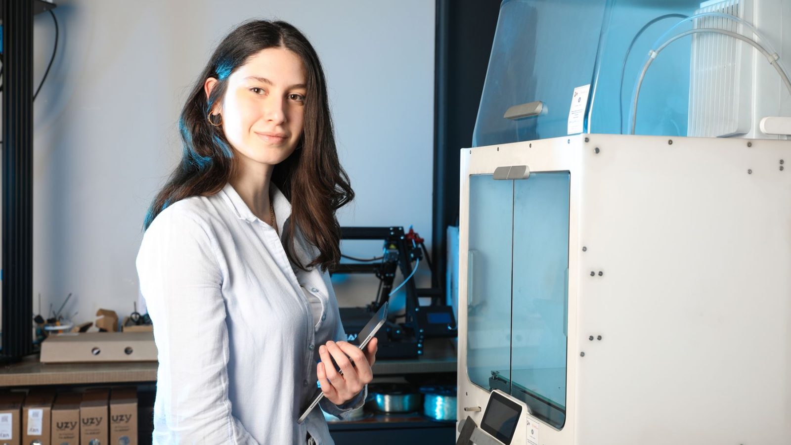 Selbstbewusste junge Ingenieurin mit Tablet neben einem 3D-Drucker in einem modernen Innenraum