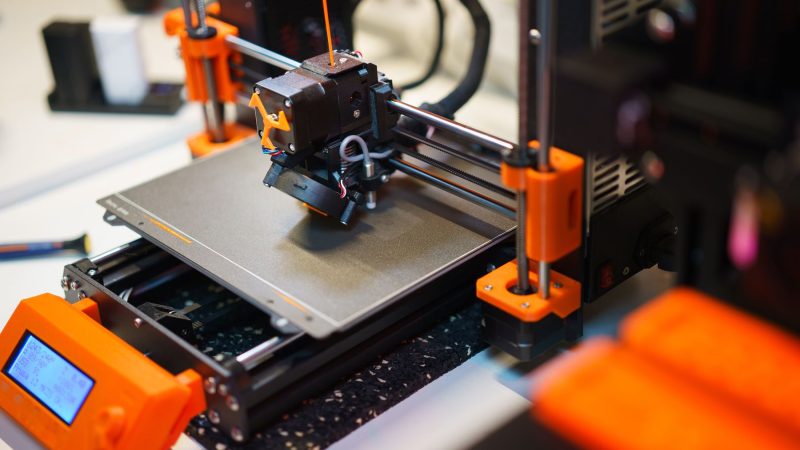 Detailansicht eines 3D-Druckers beim Drucken eines Objekts mit orangefarbenen Komponenten