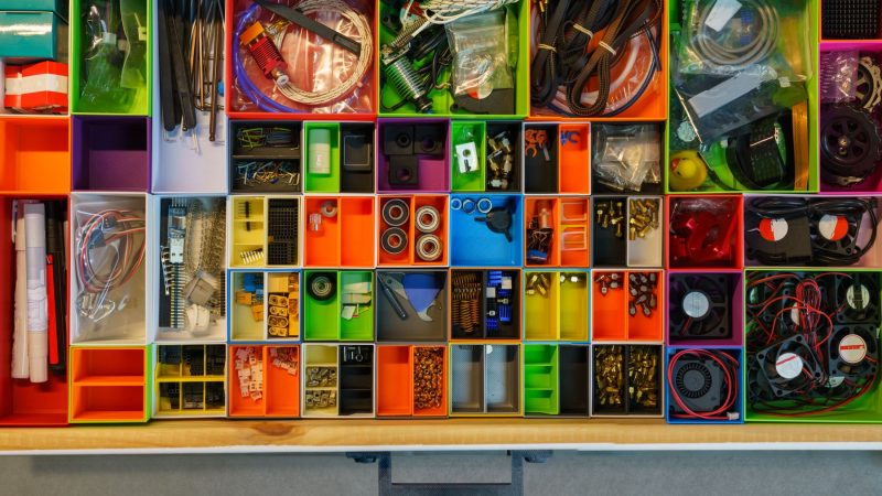 Top view of a neatly organized drawer filled with colorful containers holding various tools and electronic parts