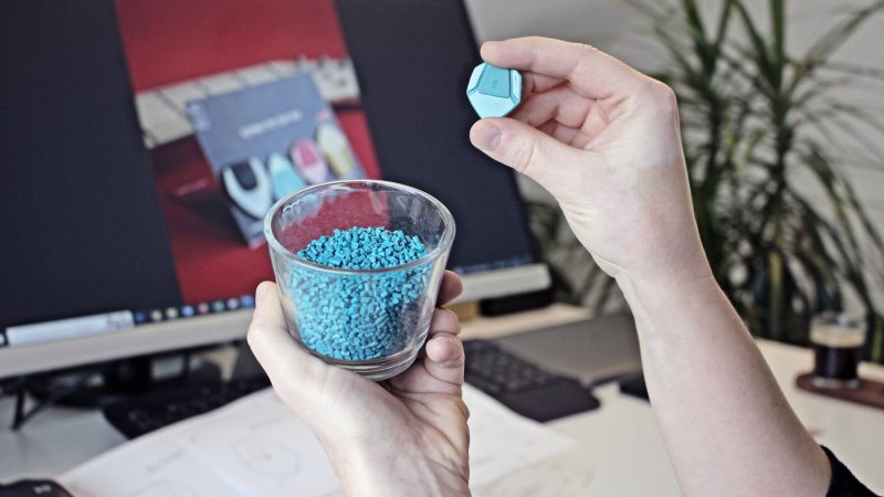 Hände halten Kunststoffgranulat, im Hintergrund ein Computerbildschirm, als Beispiel für 3D-Druck-Materialien