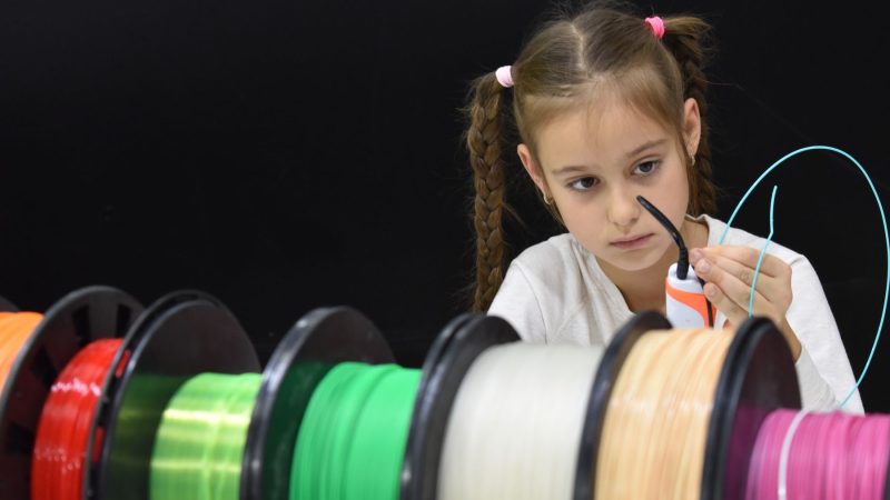 Ein konzentriertes Mädchen mit Zöpfen entdeckt den 3D-Druck mit bunten Filamenten