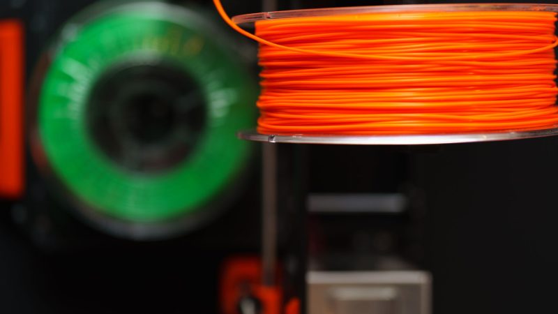 Detailed view of orange and green 3D printer filament spools, perfect for creative and industrial projects